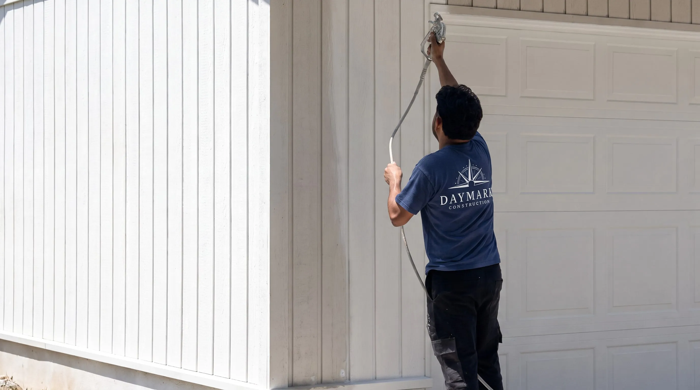 A Daymark crew member spraying the trim of a freshly painted house beside the garage door.