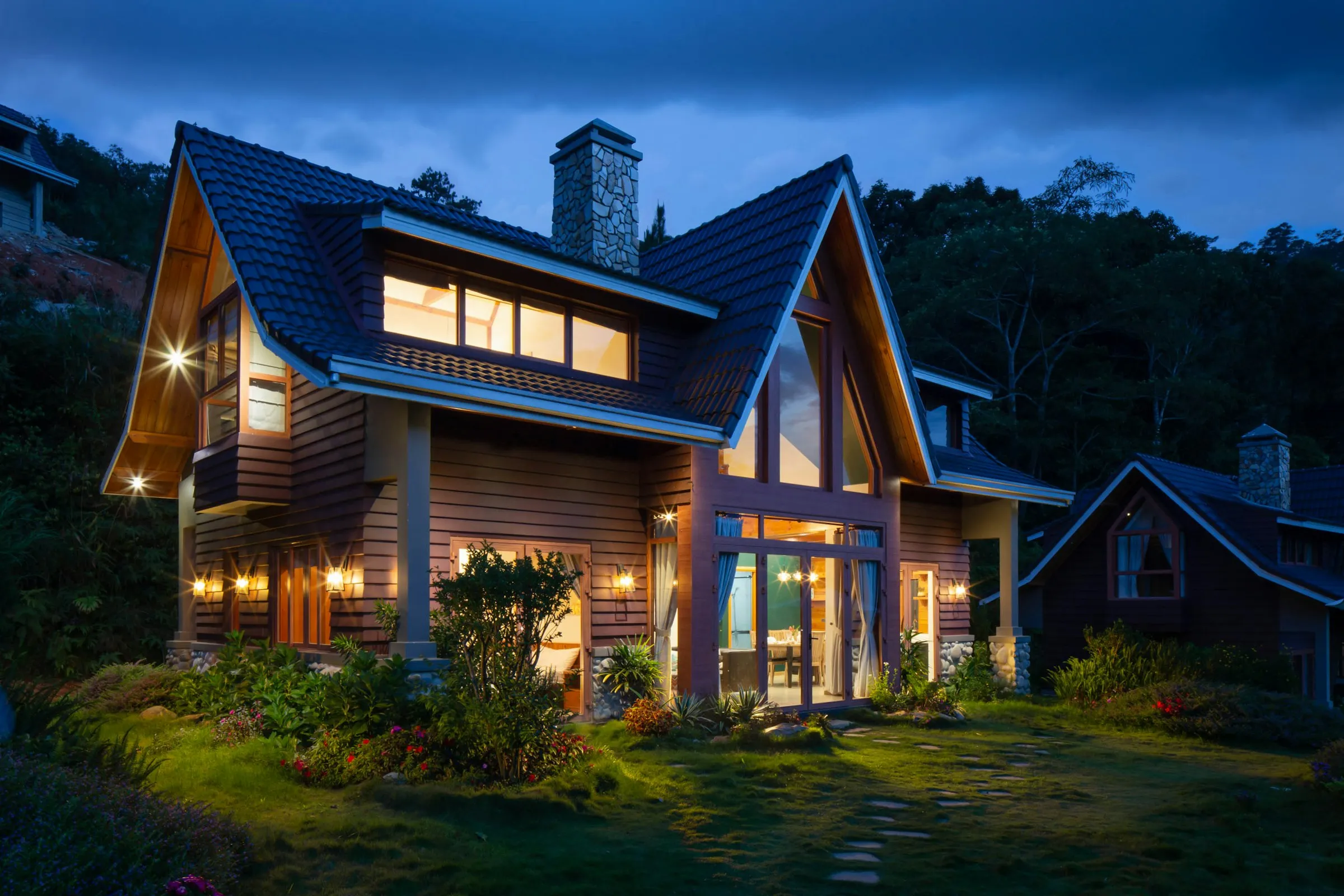 A gabled house at dusk, every window warmly lit, seen across the yard.