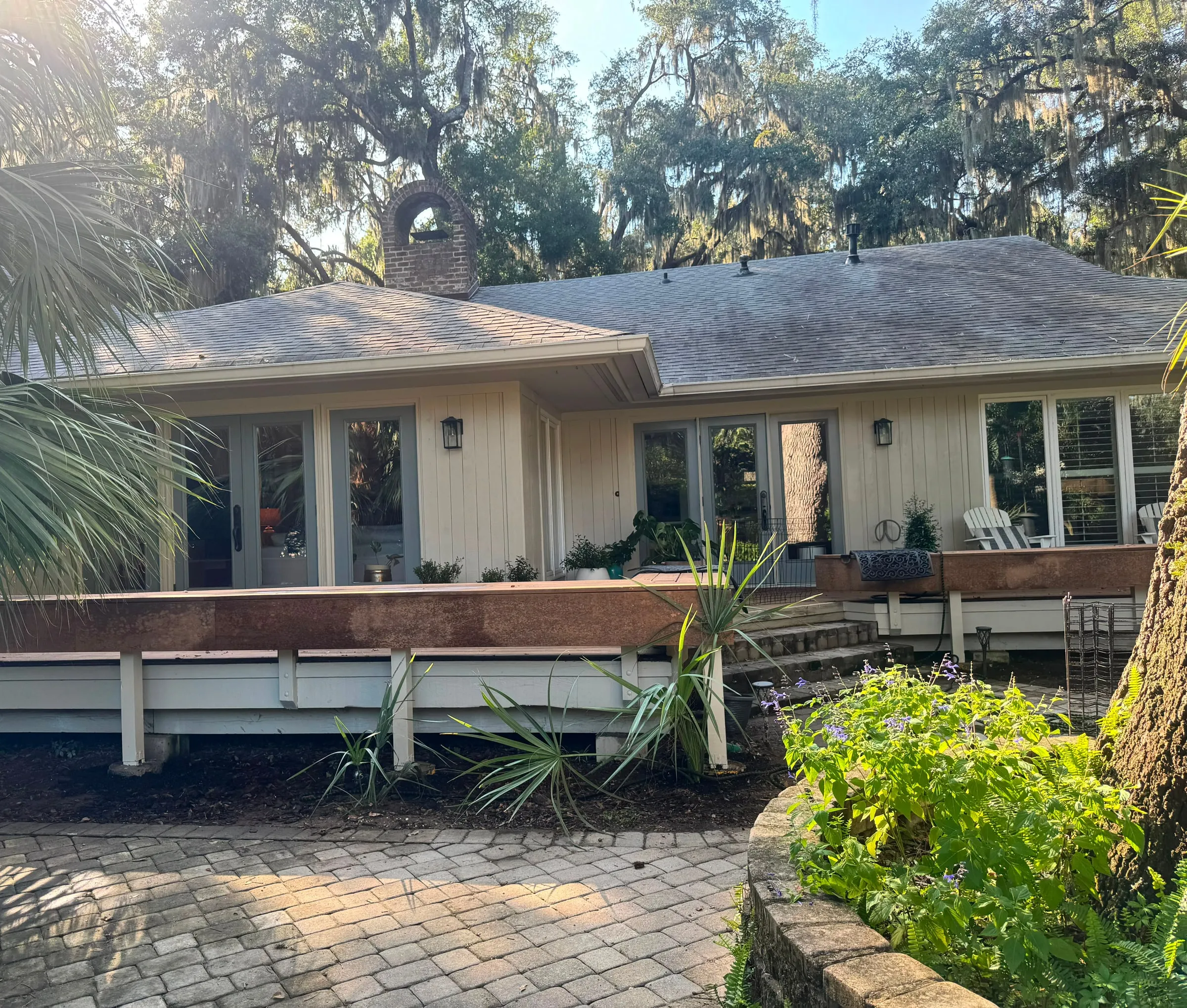 The long elevation of a single-storey house under live oaks, with the deck bench running its length.
