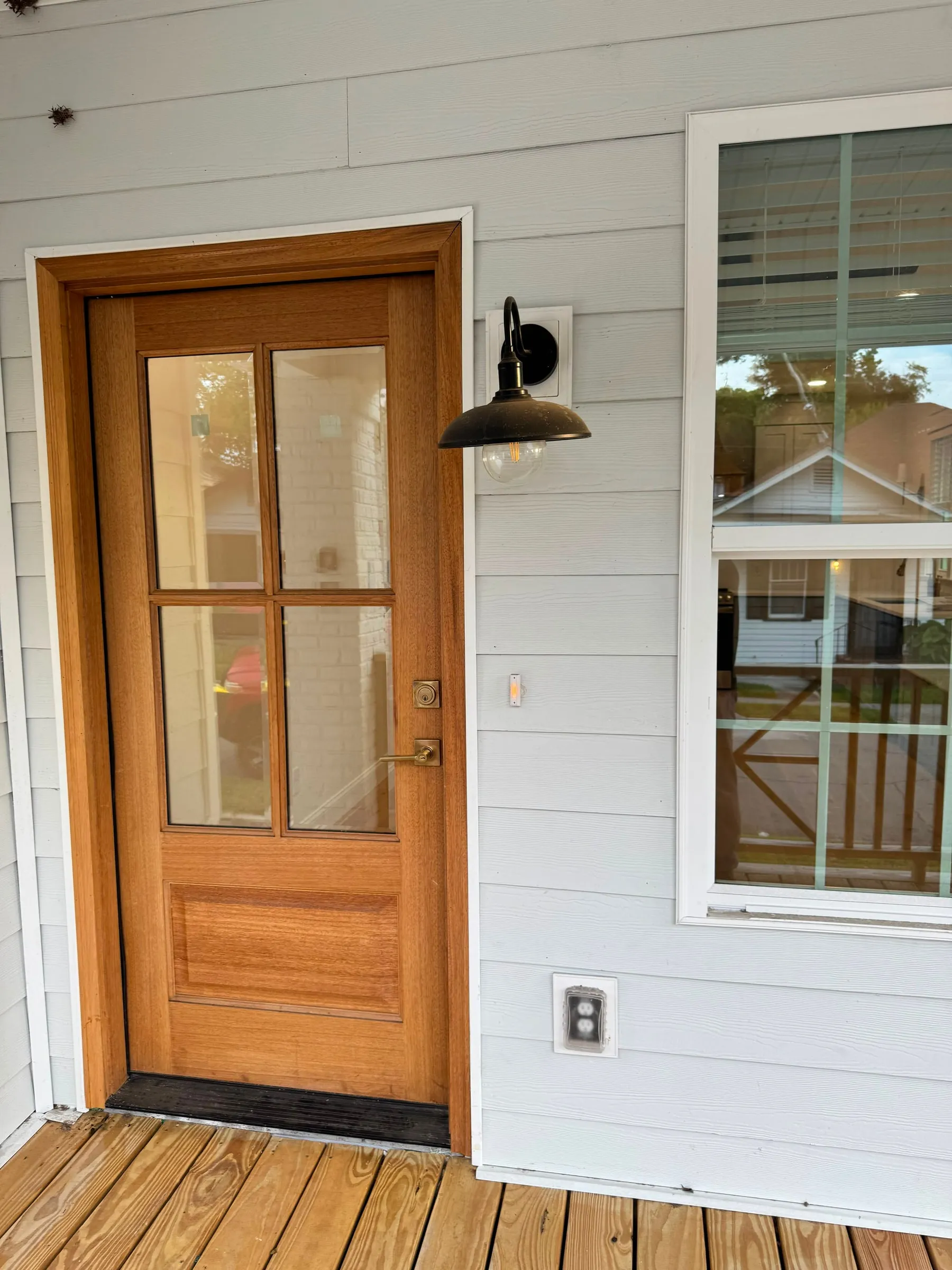 A mahogany four-light entry door beside a black gooseneck sconce and new porch decking.