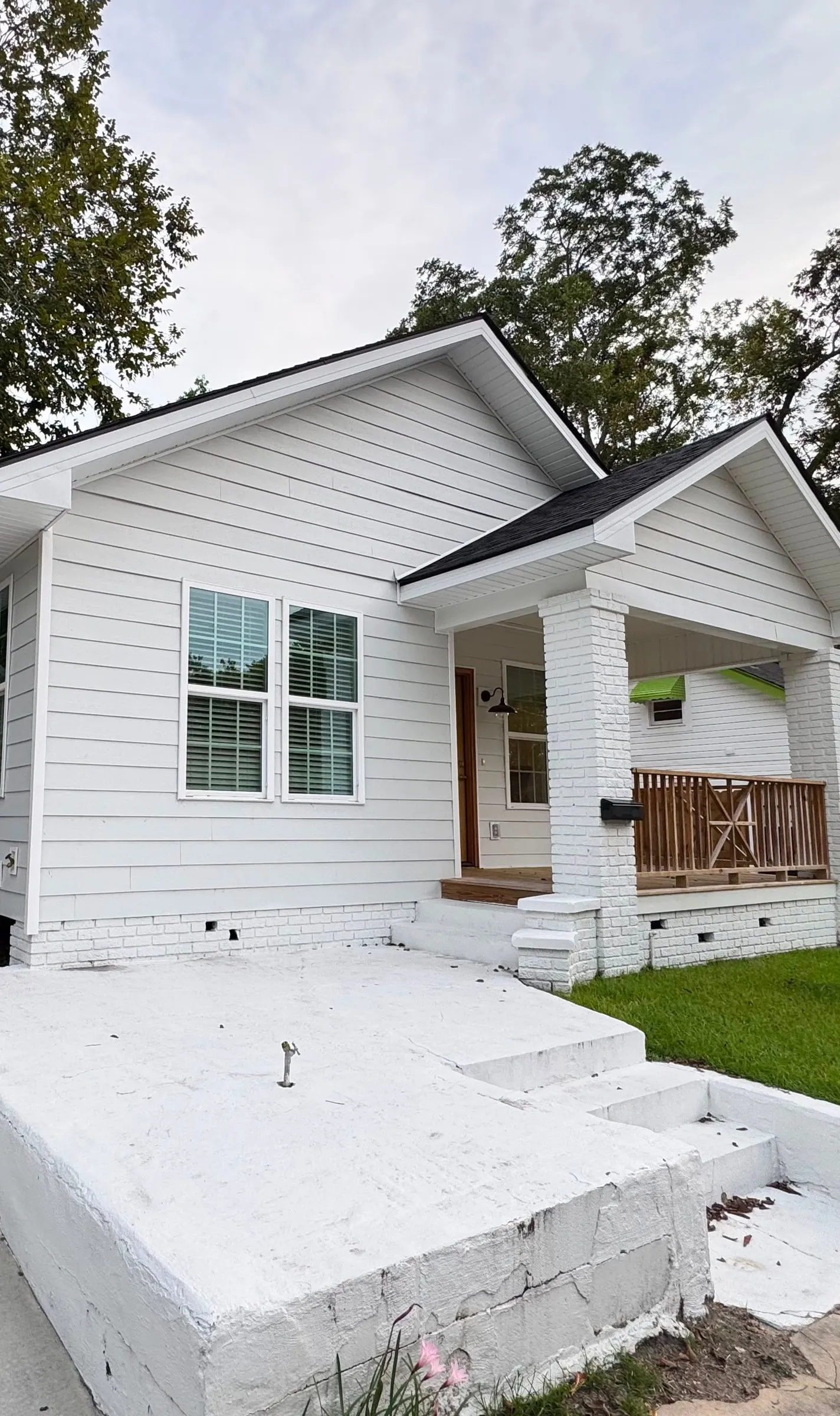 The renovated front elevation, a white bungalow with a gabled porch on painted brick piers.