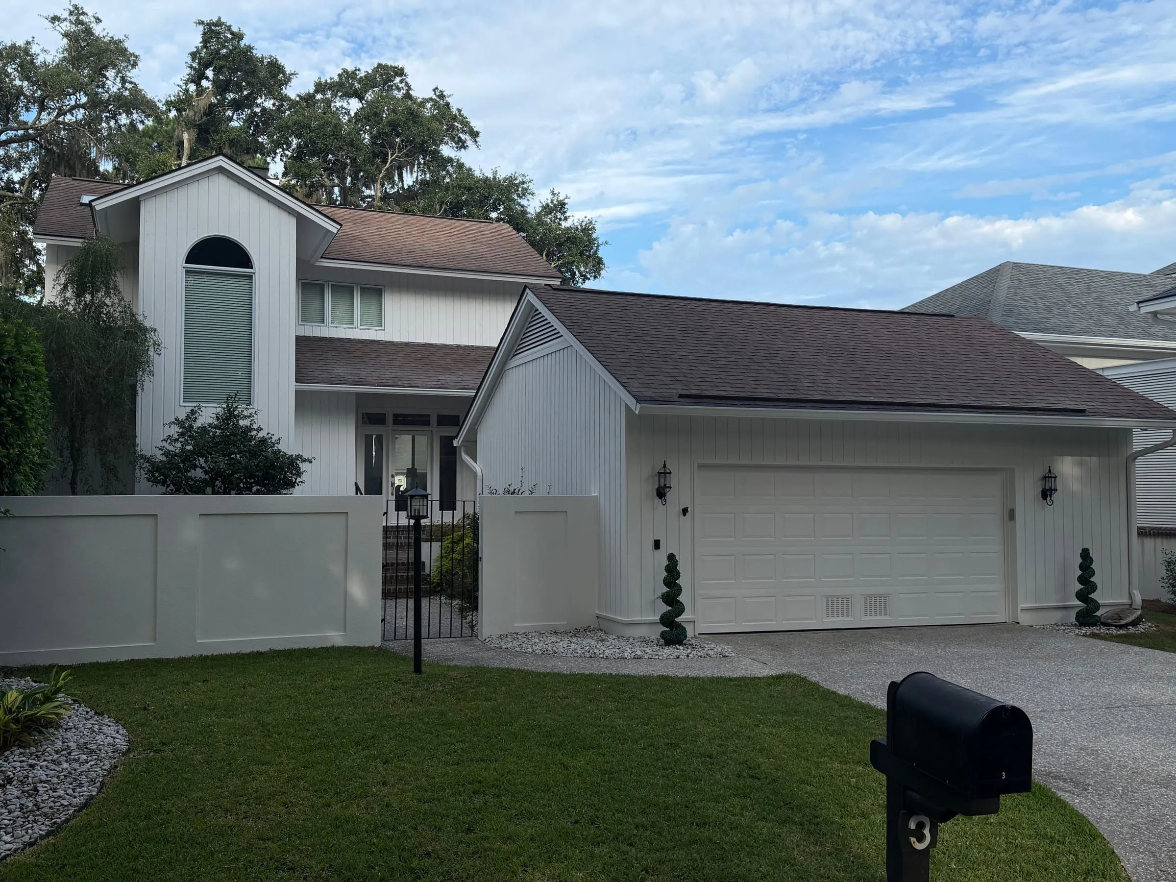 The street elevation: courtyard wall, garage, arched window in the gable, and a clipped lawn.