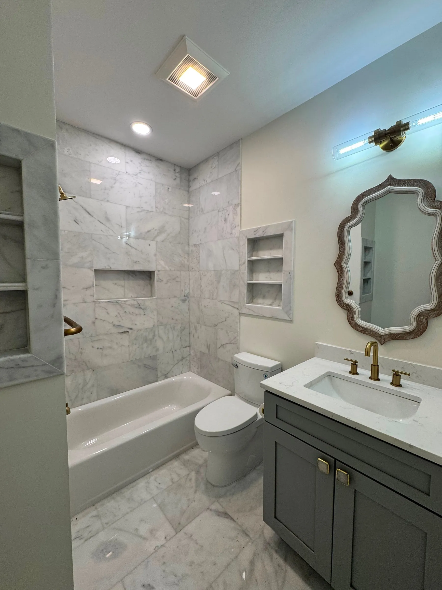 One of the new bathrooms, with a marble tub surround, recessed niches and a shaped mirror.