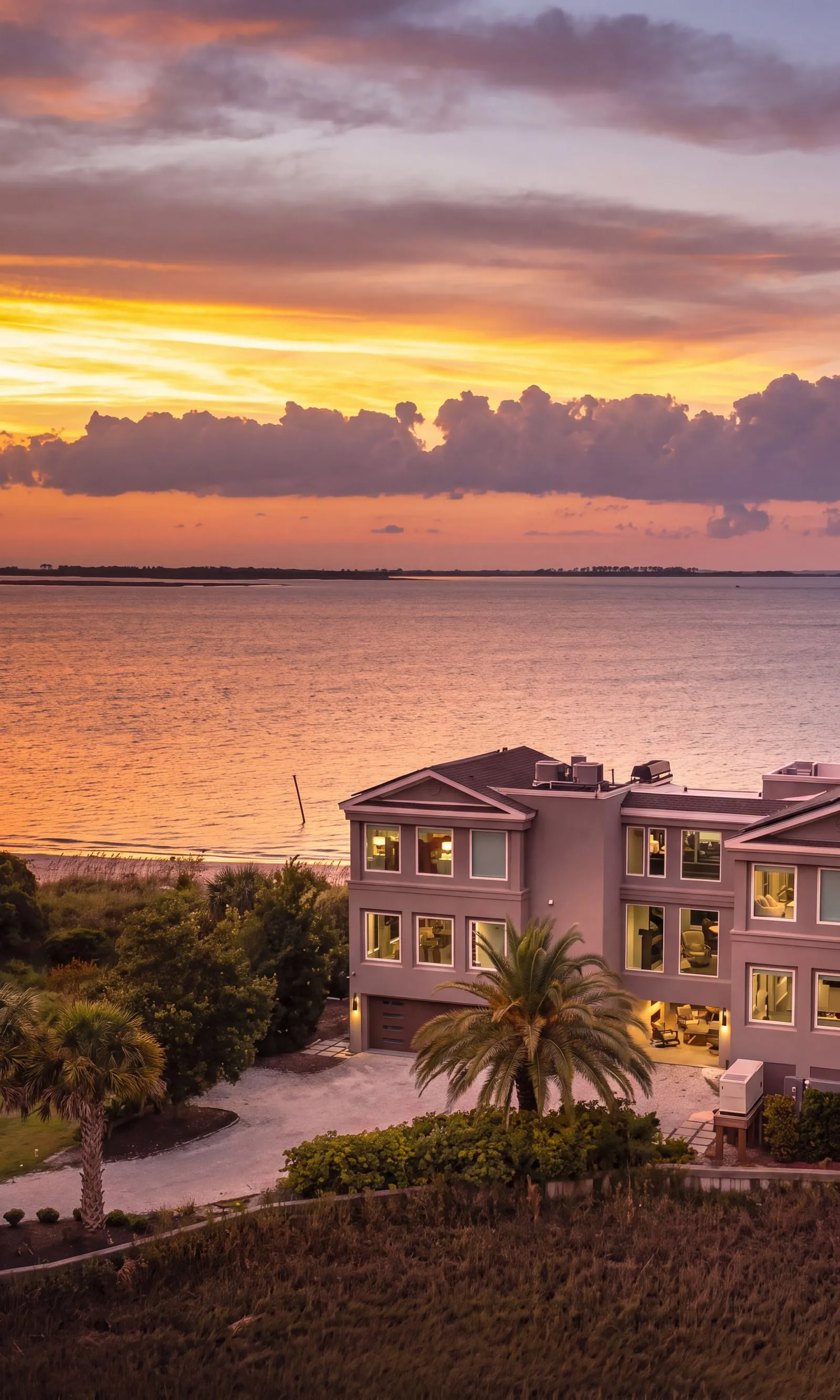 A coastal Georgia house at sunset, its windows lit above the water and marsh.