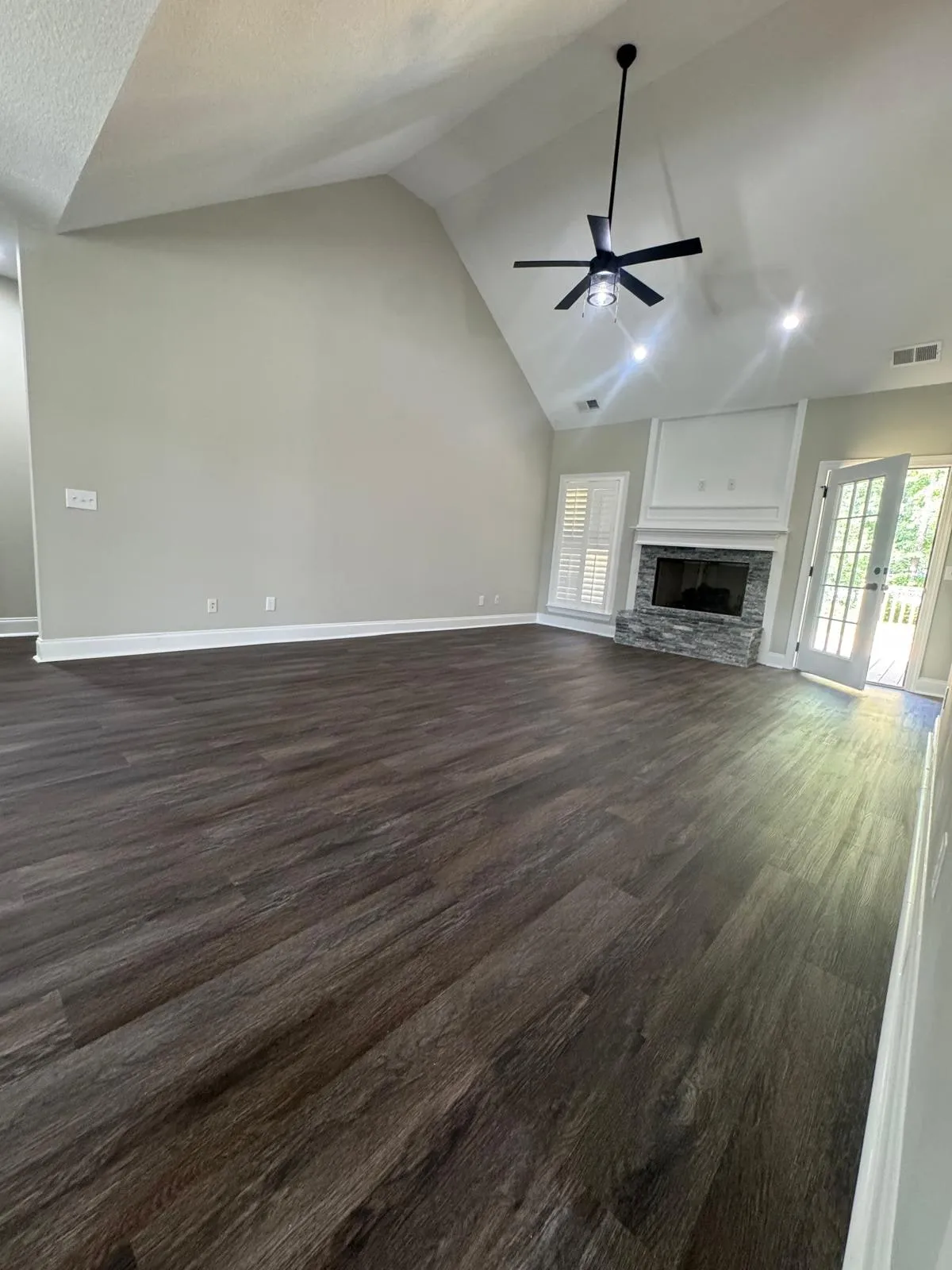 A living room under a vaulted ceiling, with a tiled fireplace and new flooring throughout.