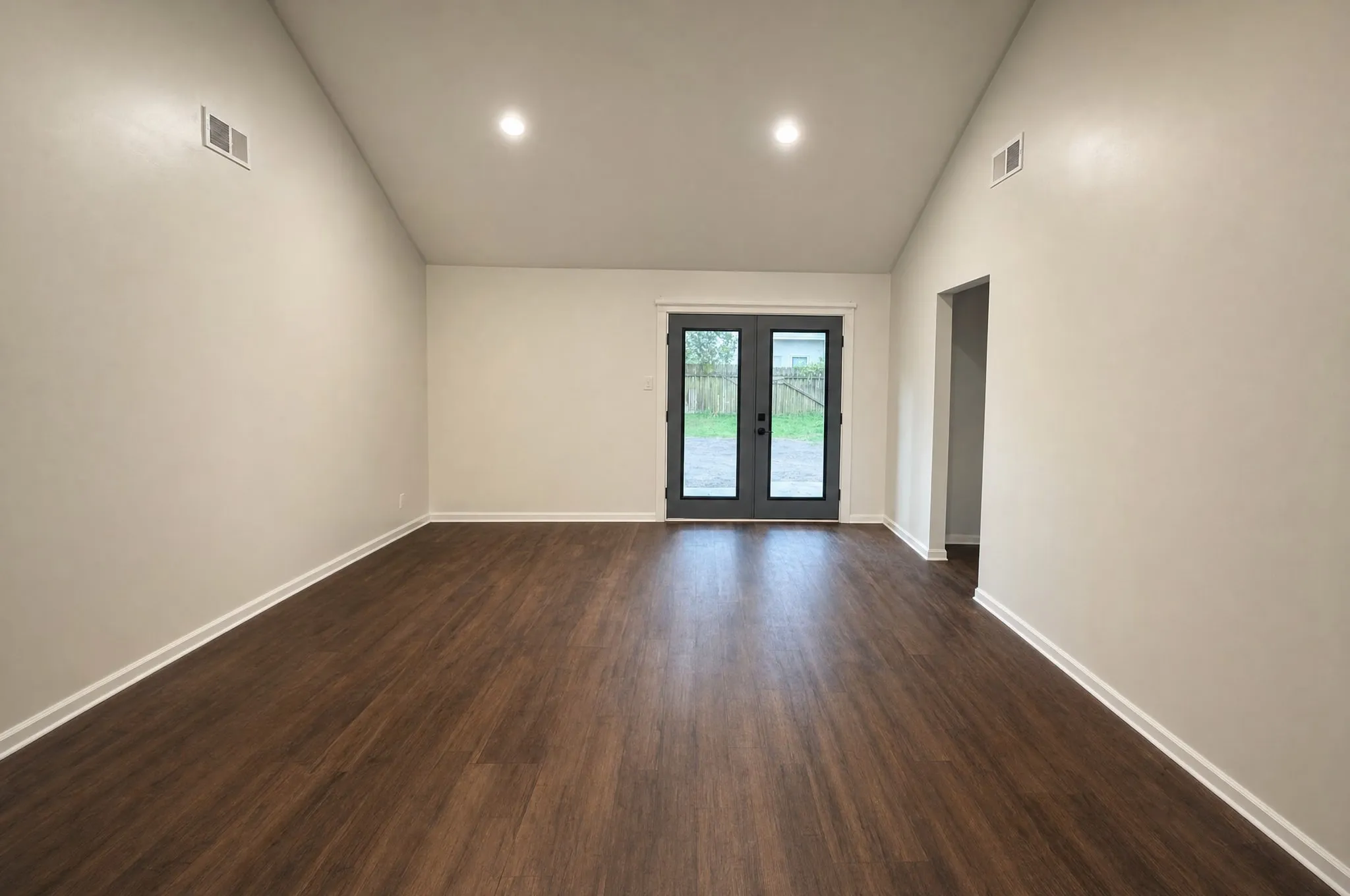 A living room after refurbishment, with French doors to the garden and new dark plank flooring.