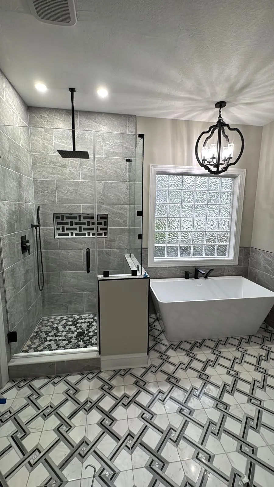 A remodelled primary bathroom with a freestanding tub, glazed shower and a glass-block window.