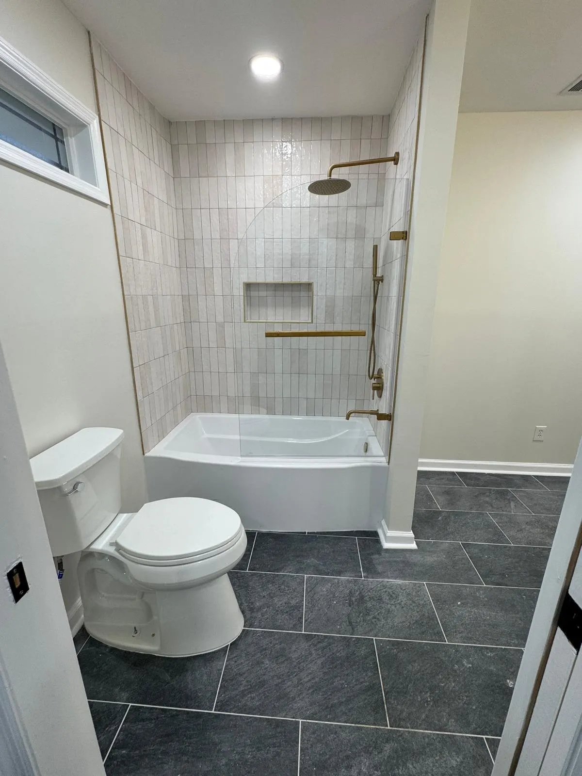 A tub and shower combination tiled floor to ceiling, with a recessed niche and brass fittings.
