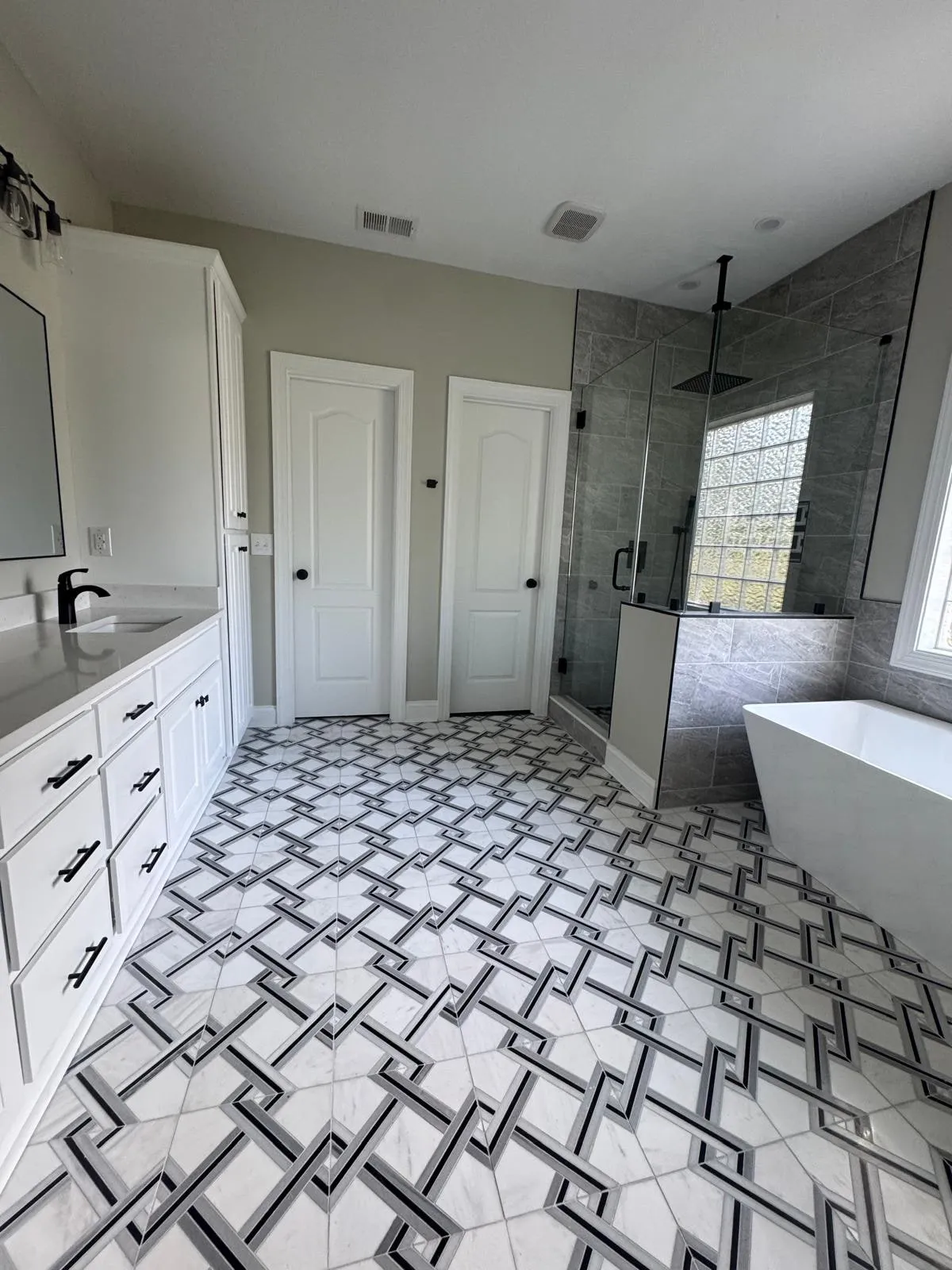 A bathroom vanity beside a custom geometric tile floor, with the shower and tub beyond.